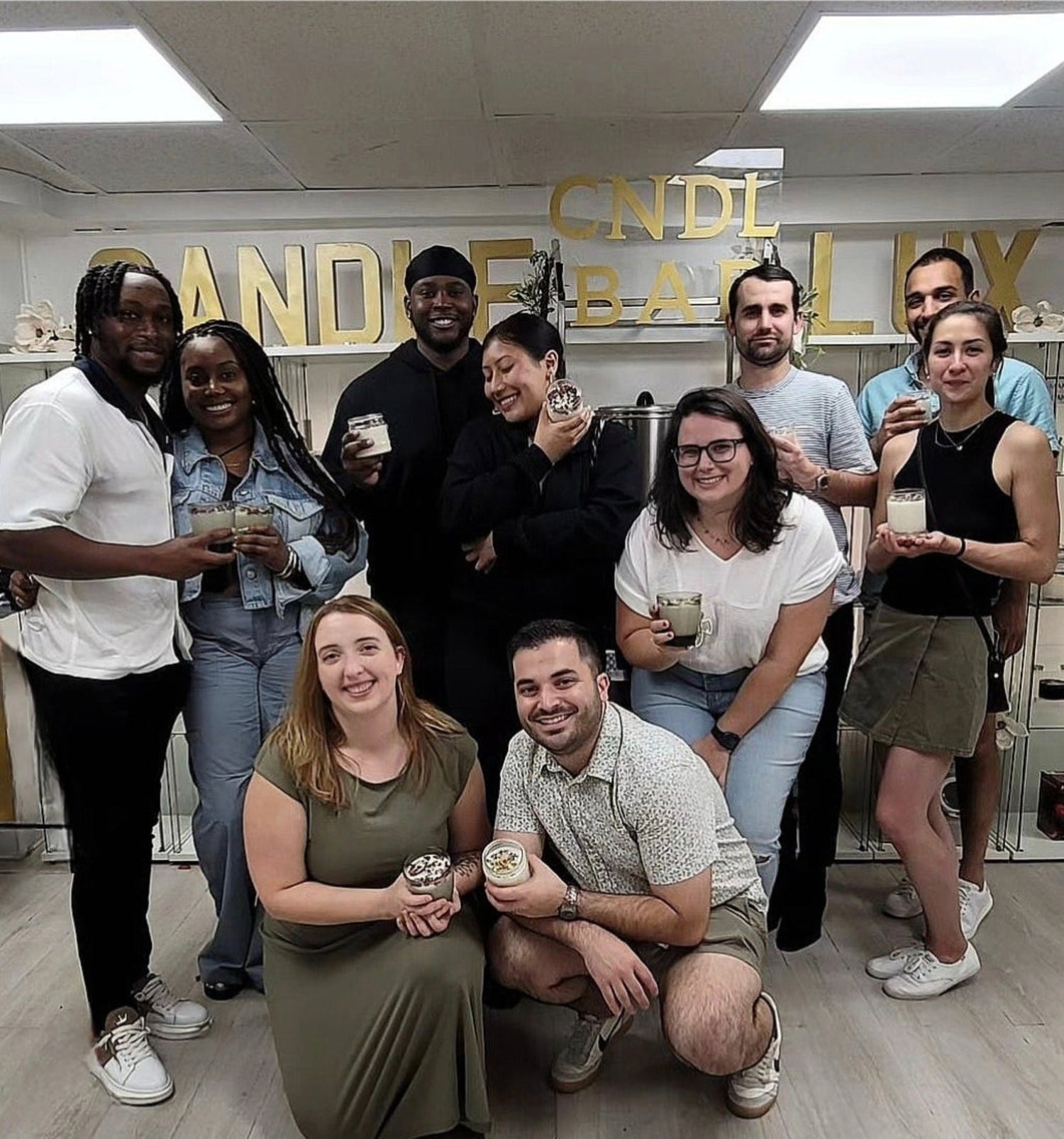 Candle-making workshop in Boston with group of people smiling and holding their candle creations.