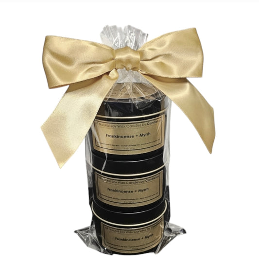 Three 4oz mini black candle tins stacked on top of eachother wrapped in a cellophane bag with a gold bow tied on the top.