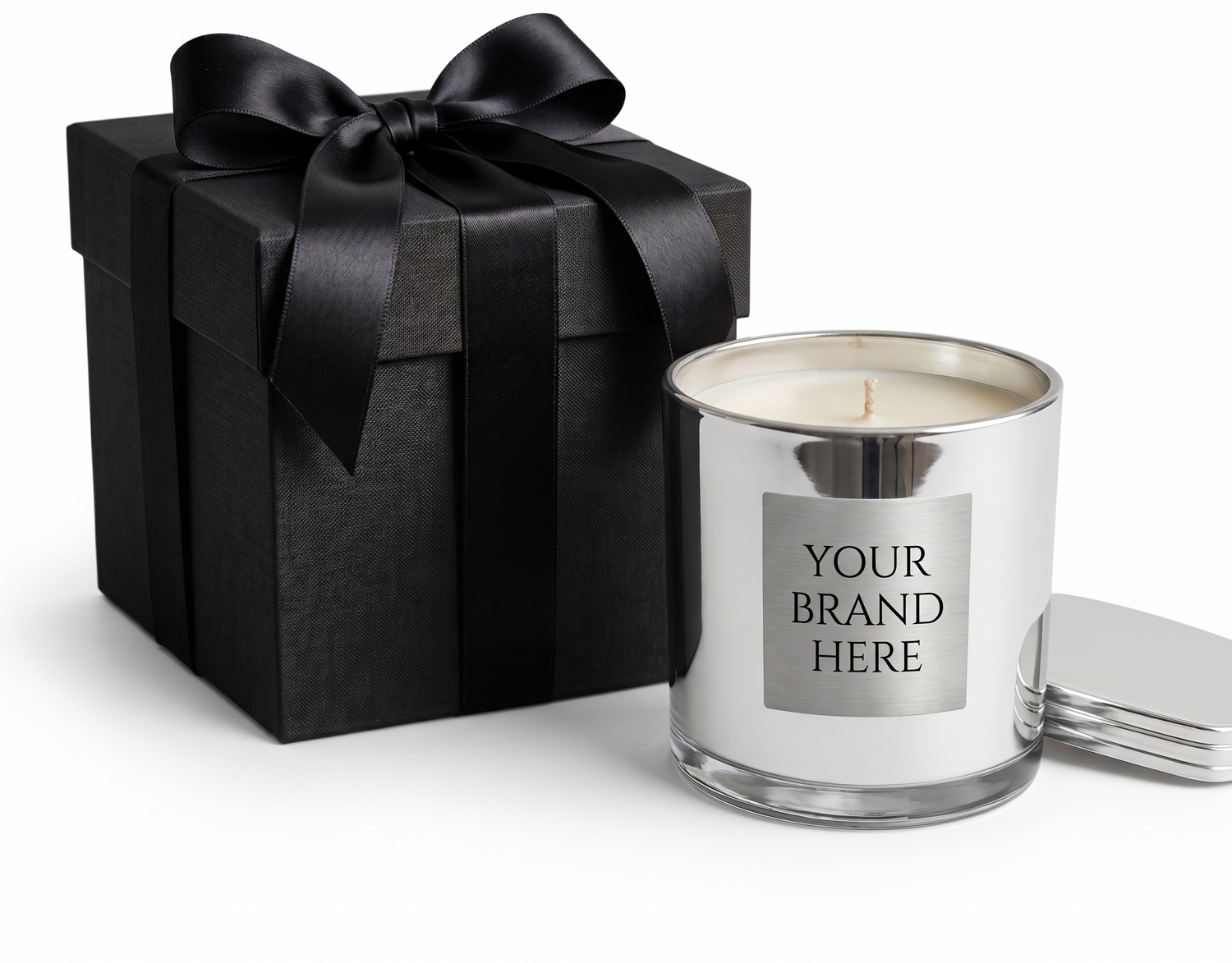 A luxury silver metallic candle jar with a silver label reading "YOUR BRAND HERE" next to a premium matte black gift box with a satin bow, perfect for custom corporate gifting.